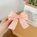 Detailed view of a soft pink satin bow hair clip held in hand with a silk texture - Orange Pink