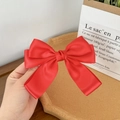 Close-up of a large red satin ribbon bow hair clip with elegant layered silk texture - Red