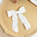 Detail of white textured fabric bow hair clip with long ribbons on a wooden tray - White