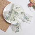 Détail du nœud à cheveux en dentelle blanche avec broderie florale sur une assiette - Style de Vigne Bleue et Verte
