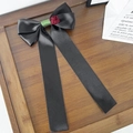 Detalle de un lazo para el pelo en satén negro con rosa roja sobre bandeja de madera - Negro