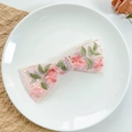 Dettaglio del fermaglio a fiocco con ricamo floreale rosa su organza in un piatto bianco - Stile Ricamato in Pizzo-Rosa