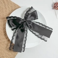 Close-up of black lace and satin bow hair clip on a white decorative ceramic plate - Black