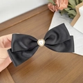 Detail einer schwarzen Satin-Haarschleife mit herzförmiger Perlenverzierung in Gold - Schwarz