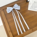 Détail de barrette à nœud bleu clair avec longs rubans soyeux sur plateau bois - Bleu