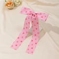 Detail of pink satin bow hair clip with red heart patterns on a soft beige background - Pink
