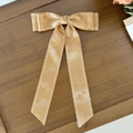 Detail of champagne gold bow hair clip with floral jacquard texture on wood background - Khaki