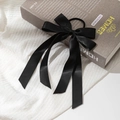 Detalle de un elegante coletero de satén negro con cintas largas sobre un libro decorativo - Negro