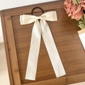 Detalle de coletero con lazo crema y cintas largas sobre una superficie de madera - Beige