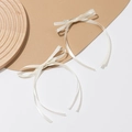 Détail d'une paire de barrettes nœuds en satin crème avec de longs rubans fluides - Beige