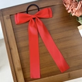 Vue détaillée d'un chouchou en satin rouge avec long ruban sur un plateau en bois - Rouge