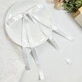 Elegante pinza de pelo de satén blanco con doble lazo y cintas largas sobre un plato - Blanco