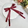 Close-up of a deep red double-layered satin bow hair clip with long ribbons on a white plate - Burgundy