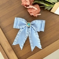 Close-up of light blue silk bow hair clip with a heart-shaped teal gemstone and gold base - Blue
