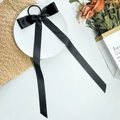 Close-up of black satin long ribbon bow hair tie with silky texture on ceramic plate - Black