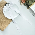Macro detail of a white satin long ribbon bow scrunchie on a decorative white plate - White