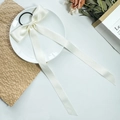 Close-up of cream satin bow hair tie with long ribbons in a minimalist ceramic dish - Beige