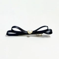 Detail of a black satin bow hair clip featuring a heart pearl centerpiece and metal clip - Black