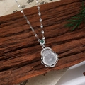 Détail macro du pendentif Bouddha avec zircon blanc et chaîne argentée sur fond de bois zen - Style Bouddha E