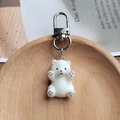 Cute white flocked polar bear keychain with silver metal clasp on a wooden tray - Lying Polar Bear