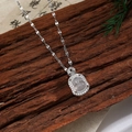 Détail d'un pendentif bouddha argenté avec zircons sur fond de bois sombre et pins - Style Bouddha G