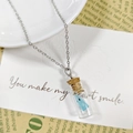 Détail d'un pendentif en bouteille de verre avec fantôme bleu sur carte à motifs de roses - Collier Bleu