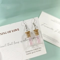 Vue macro de boucles d'oreilles bouteille en verre avec liège et fantôme rose brillant - Boucles d'oreilles roses