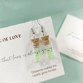Gros plan de boucles d'oreilles bouteille en verre avec mini fantôme lumineux - Boucles d'Oreilles Vertes