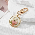 Detailed view of dried pink daisy flowers encased in a clear resin round gold keychain - Pink Daisy White Gypsophila