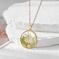 Détail macro du collier pendentif rond en or avec de vraies fleurs séchées blanches - Marguerite Blanche Gypsophile Blanche