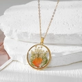 Détail macro du collier pendentif rond doré avec de vraies fleurs séchées et pétales blancs - Marguerite Orange Gypsophile Blanche