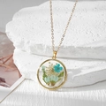 Vue détaillée du pendentif rond en résine avec fleurs séchées et cadre doré - Marguerite Bleue Fleur Bleue Gypsophile Blanche