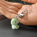 Close-up of a green flocking chick keychain plush held by hand with a metal lobster clasp - Curly Tail Green Snake