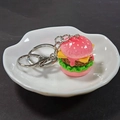 Detail of a 3D resin pink burger keychain with layered cheese and metal clasp on a white plate - Pink 3D Hamburger