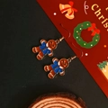 Detail shot of a gingerbread man earring with blue and brown enamel on a festive backdrop - Gingerbread Man