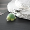 Cute green flocking turtle keychain with silver metal hook on a white textured stone - Matcha Turtle