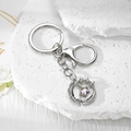 Detailed close-up of silver hollow moon wreath keychain with aurora gemstone on stone - Silver Feather