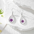 Gros plan de boucles d'oreilles en résine goutte avec de vraies fleurs séchées violettes - Une Seule Fleur Violette