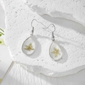 Gros plan de boucles d'oreilles artisanales en résine avec de vraies fleurs séchées jaunes - Une Seule Fleur Jaune Clair