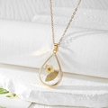 Élégant collier goutte en résine dorée avec fleurs séchées sur un présentoir blanc - Fleur Blanche avec Feuilles Vertes