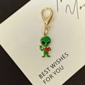 Nahaufnahme eines grünen Alien-Anhängers mit rotem Herz und goldenem Karabinerverschluss - Herz-Alien Großer Hummerverschluss