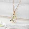 Macro detail of teardrop resin pendant with purple dried flowers on a gold chain - Two-leaf Holly