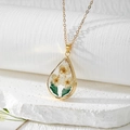 Macro detail of teardrop resin pendant with real dried flowers and gold leaf accents - Three White Flowers