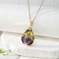 Detailed close-up of a teardrop resin pendant with real purple and yellow dried flowers - Pansy