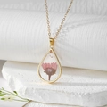 Close-up of teardrop resin pendant featuring pink dried flower and gold foil flakes - Pink Daisy