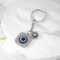 Macro shot of silver alloy Evil Eye keychain with shimmering rhinestones on white stone - Silver Square Eye