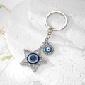 Star-shaped evil eye keychain with blue crystal charms on a white stone background - Silver Star Eye