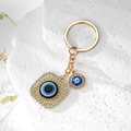 Detailed macro of golden Evil Eye keychain with sparkling crystals on a white stone background - Gold Square Eye