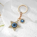Close-up of golden star and circle evil eye charms with sparkling crystals on white stone - Gold Star Eye