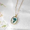 Détail du pendentif ovale en résine avec fleur séchée bleue et perle sur un cadre doré poli - Fleur Bleue Feuilles Vertes Perle Artificielle